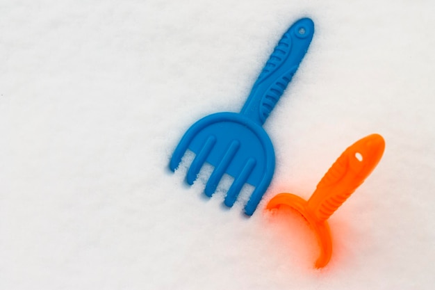 Kinderspeelgoed in de sneeuw. Plastic blauwe hark van kinderen in de sneeuw en een gele schop.