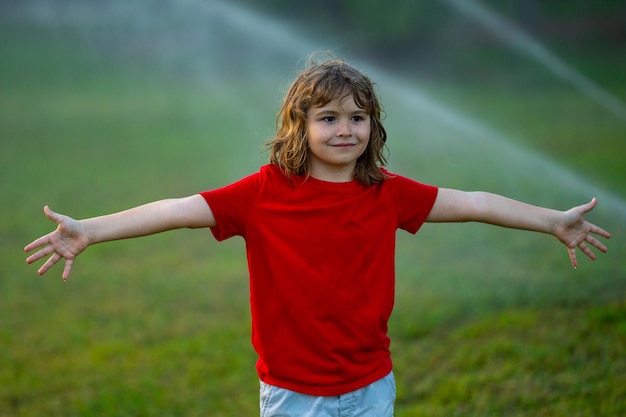 Kinderspel in het gras van de zomertuin dat automatisch sproeiirrigatiesysteem in een groen park water geeft