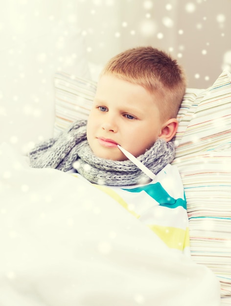 kindertijd, gezondheidszorg en geneeskundeconcept - zieke jongen met thermometer die in bed ligt en thuis temperatuur meet