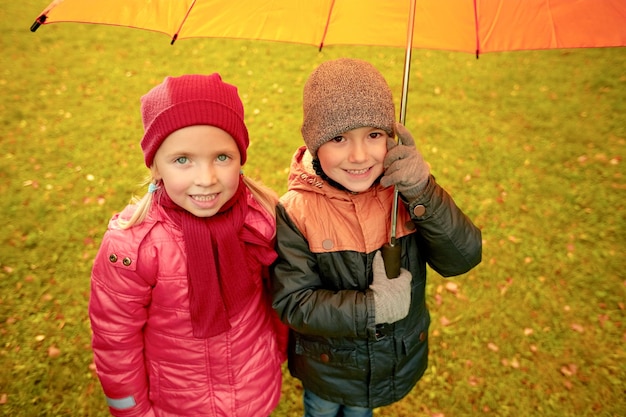 kindertijd, vriendschap, seizoen, weer en mensenconcept - gelukkig jongetje en meisje met paraplu in herfstpark