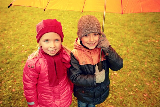 kindertijd, vriendschap, seizoen, weer en mensenconcept - gelukkig jongetje en meisje met paraplu in herfstpark