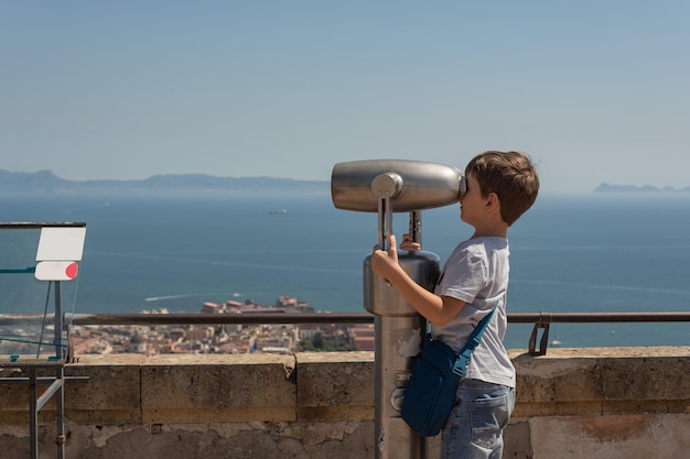 Kindertoerisme in Europa Kleine jongen met verrekijker kijkend naar de stad Napels, Italië Het kijkt naar de bergen en de Vesuvius