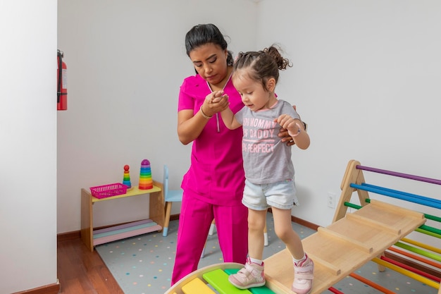 Kinderverpleegkundige helpt een meisje door een houten spel te lopen in haar medische kantoor