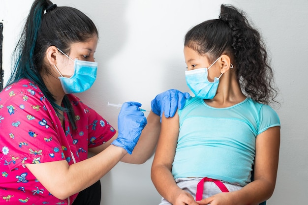 Kinderverpleegster die arm van klein bruin meisje injecteert, doktershanden met rubberen handschoenen