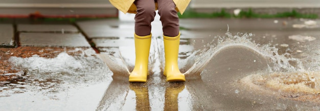 Kindervoeten in gele rubberen laarzen springen over een plas in de regen