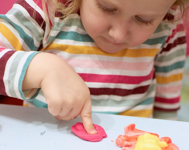 Kindhanden die met kleurrijke klei spelen. Plasticine. deeg spelen, quarantaine op sociale afstand Covid-19, zelfisolatie, online onderwijsconcept, thuisonderwijs. Peutermeisje thuis, kleuterschool gesloten.