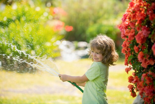 Kindjongen die de planten water geeft van slangspray met waterslang in de tuin in de achtertuin van de h