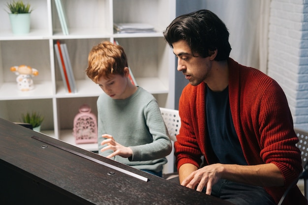 Kindjongen die thuis synthesizer speelt tijdens de lesmuziekleraar die in de buurt zit en helpt