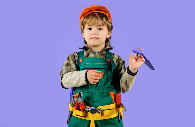 Kindjongen in bouwersuniform met gereedschapsriemgereedschap voor het bouwen van een klein kind in overall en veiligheid