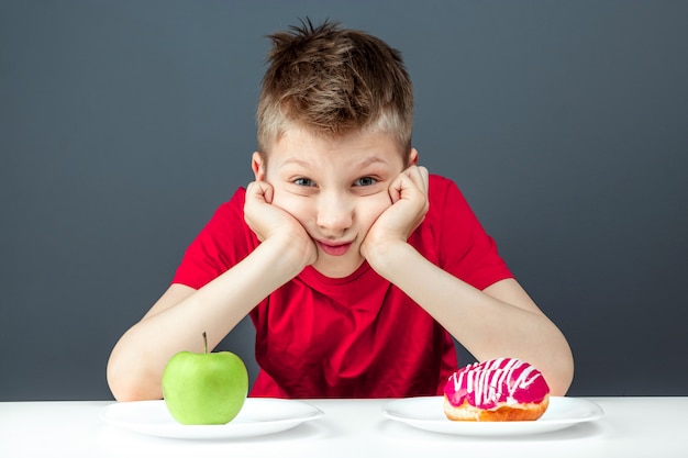 Kindjongen kiest tussen een donut en een groene appel. Concept Weerstand tegen verleiding, fast food, gezonde voeding, dieet.