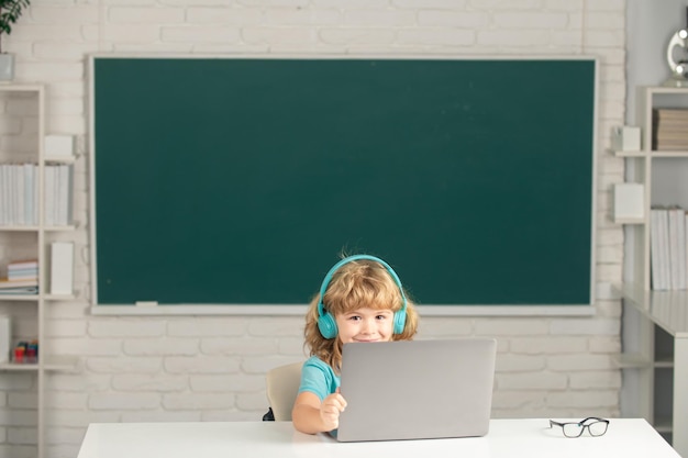 Kindjongen met koptelefoon die een laptop gebruikt en online studeert met een videogesprekleraar op de basisschool