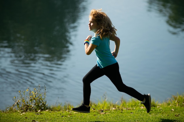 Kindjongen rennen of joggen in de buurt van meer op gras in park sportieve jongensloper rennen in zomerpark act