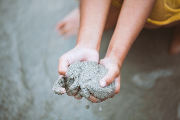 Kindmeisje bedrijf zand in handen en spelen op het strand in de zomervakantie