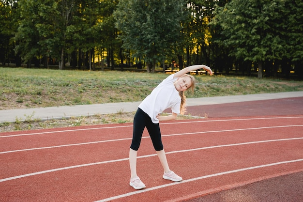 Foto kindmeisje dat rekoefeningen doet voordat ze op een sportbaan rent