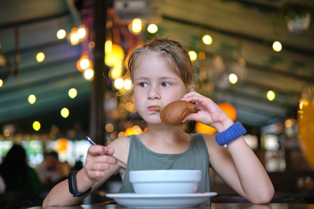 Kindmeisje dat soep en smakelijke hamburger eet in restaurant.