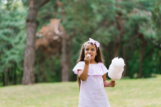 Kindmeisje eet suikerspin op een zonnige zomerdag en likt plakkerige vingers Lopen met kinderen in het park op vakantie