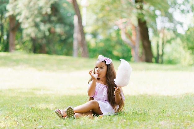 Kindmeisje eet suikerspin op een zonnige zomerdag en likt plakkerige vingers lopen met kinderen in het park op vakantie