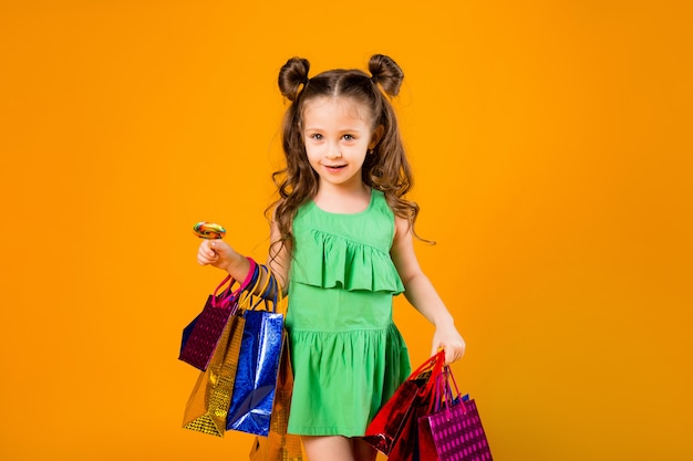 Foto kindmeisje het glimlachen die kleurrijke het winkelen zakken houden, die zich op een gele ruimte bevinden. kleine fashionista, ruimte voor tekst