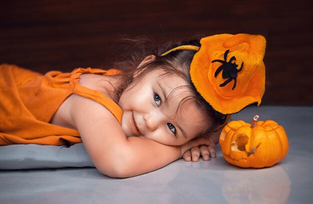 Kindmeisje ligt op de grond naast Halloween-decoratie Jack-O-Lantern