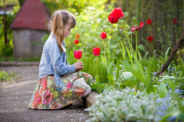 Kindmeisje openlucht bij bloembed die heldere rode tulp bekijken