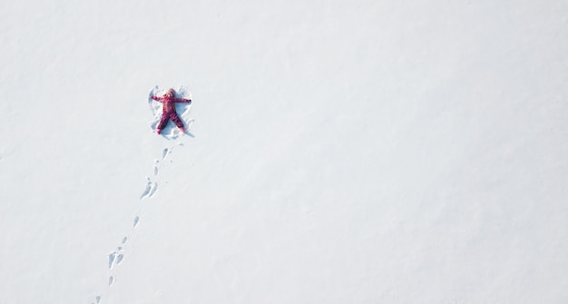 Kindmeisje spelen en het maken van een sneeuwengel in de sneeuw. Bovenaanzicht plat bovenaanzicht