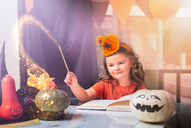 Kindmeisje verkleed als heksenkostuum een toverstaf over Halloween-pompoenen