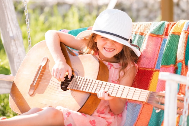 Kindmuzikant die gitaar speelt stijlvol klein kindmeisje dat een zomerjurk draagt en plezier heeft op de achtertuin