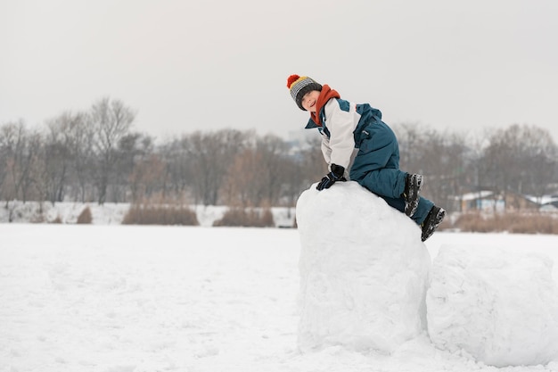 Kindspel in het sneeuwfort. Winterplezier buitenshuis. Jongen klom op stapel sneeuw.