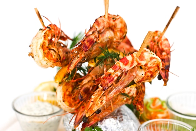 King prawns cooked on wooden skewers. Serving with sauces and herbs on a white plate.