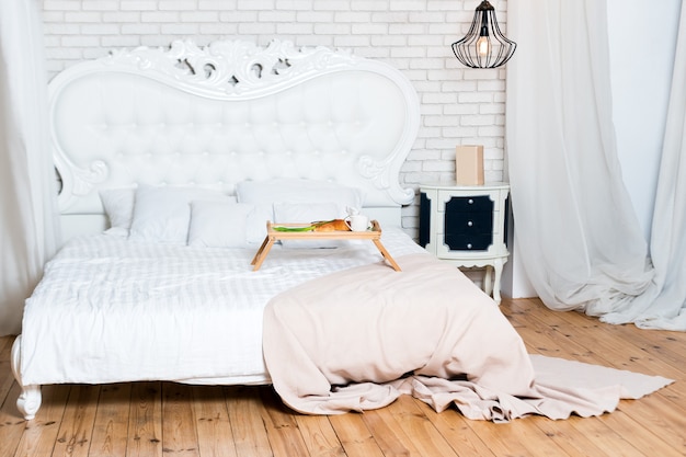 Kingsize bed in loft-appartement, ontbijt op bed, een dienblad met koffie, croissants en bloemen, huwelijksreis, vroeg in de ochtend in het hotel.