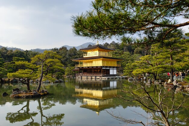 Foto kinkaku-ji tempel bij bomen met reflectie in de vijver tegen de lucht