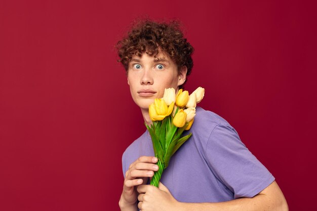 Ragazzo vizioso che tiene un mazzo di fiori gialli magliette viola sfondo rosso inalterato