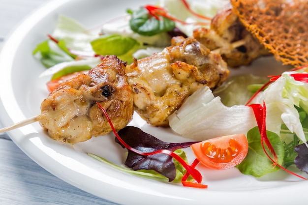 Kip gegrild vlees op stok met salade en tomaten op witte plaat