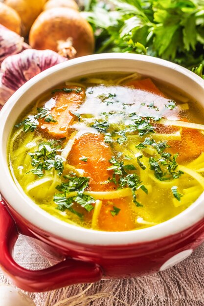 Kip- of groentesoepbouillon in een vintage bowl met huisgemaakte noedels wortel ui bleekselderij kruiden knoflook en verse groenten.