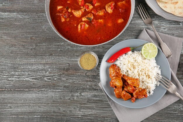 Kip tikka masala in pan en portie met rijst op grijze houten tafel