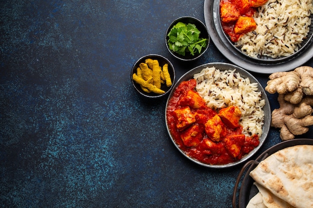 Kip tikka masala schotel met rijst, plat Indiaas brood en kruiden in rustieke metalen platen op betonnen achtergrond bovenaanzicht. Kip-tomatencurry, traditionele Indiase maaltijd, vrije ruimte voor tekst