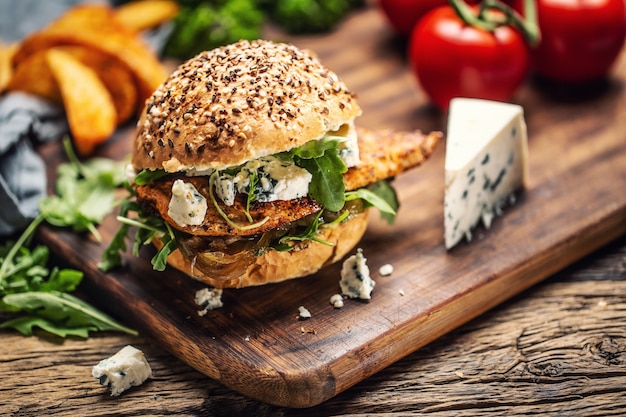 Kipburger met blauwe kaas en rucola in een sesambroodje op een rustiek hout.