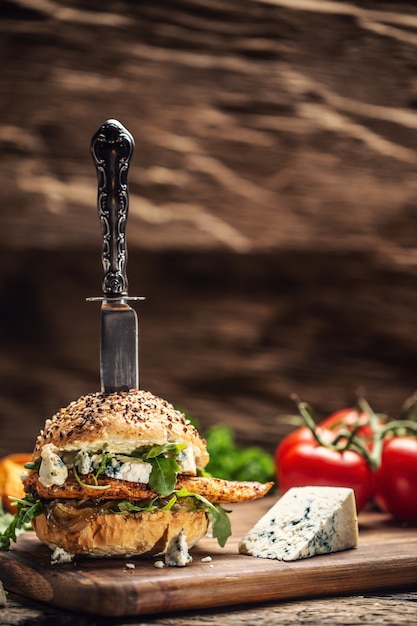 Kipburger met blauwe kaas en rucola in een sesambroodje op een rustiek hout.