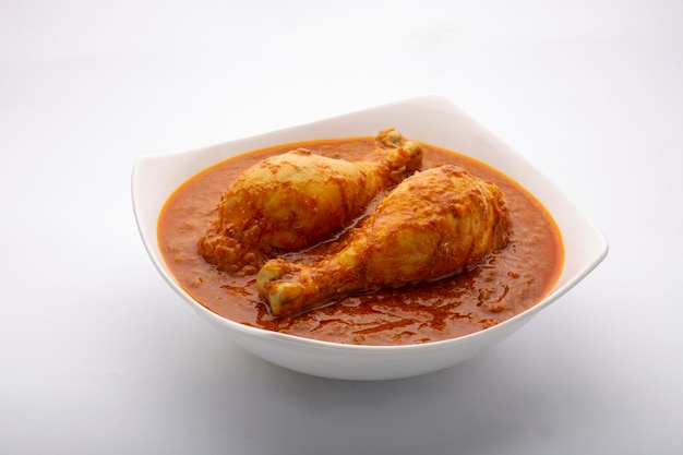 Kipcurry of masala, pittig roodachtig kippenpootstuk gegarneerd met korianderblad en verse groene chili, gerangschikt in een witte keramische kom met witte achtergrond, geïsoleerd.