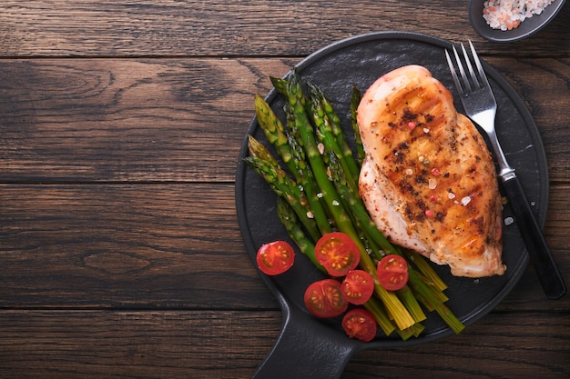 Kipfilet gegrild met groenten gegrilde kip steak asperges en kerstomaatjes in zwarte plaat op houten donkere tafel achtergrond gezonde voeding lunch barbecue steak gebakken bovenaanzicht