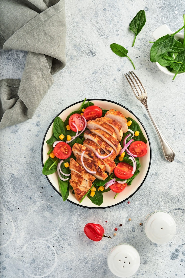 Foto kipfilet met salade spinazie, kerstomaatjes, korenbloem en ui. gezond eten. keto-dieet, dieetlunchconcept. bovenaanzicht op witte achtergrond.