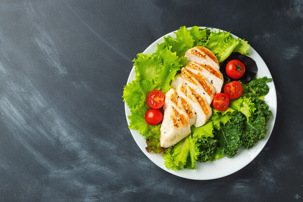 Kipfiletfilet en groentesalade met tomaten en groene bladeren. het concept van gezond voedsel en keto-dieet. bovenaanzicht.