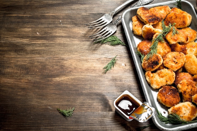 Kipnuggets op een stalen bakje met saus. Op een houten tafel.