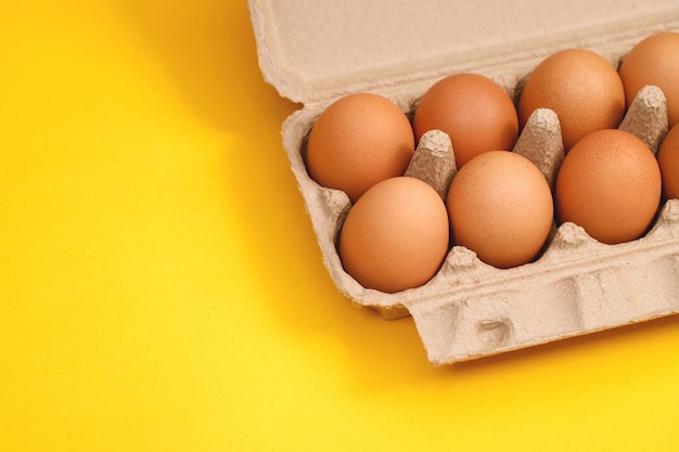 Kippeneieren in een kartonnen doos klaar om te koken op een gele achtergrond