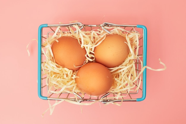 Kippeneieren in een winkelwagentje op een roze pastel achtergrond, kopie ruimte, flatlay