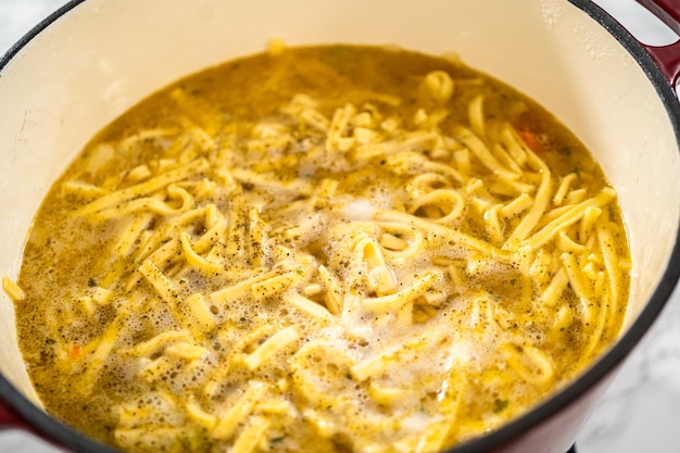 Kippennoedelsoep koken met kluski noedels in een geëmailleerde dutch oven