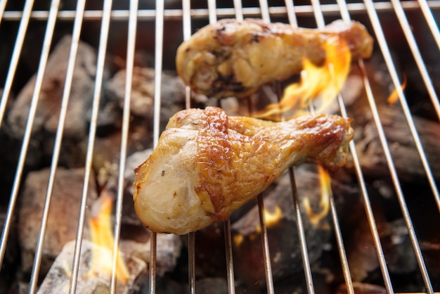 Foto kippenpoten die over vlammen op een barbecue roosteren.