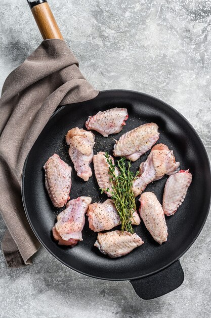 Kippenvleugels met kruiden en specerijen klaar om te koken in een pan. Grijze achtergrond. Bovenaanzicht.