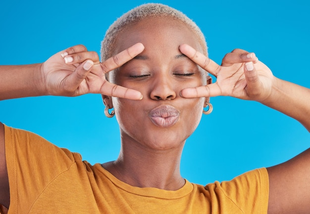 Kiss black woman and peace hands on face in studio for self love thank you or good vibes on blue background V sign and African female with cool mood pose or freedom emoji for support or swag