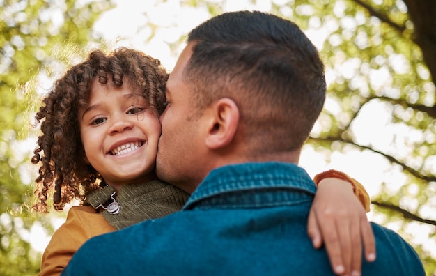 Photo kiss portrait and a child and father in nature with a hug for playing bonding or family happy together and a young dad with care love and carrying a girl kid in a park for outdoor walking